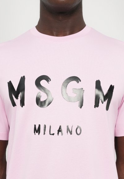 Lyserød bomulds-t-shirt med sort penselskrift, der staver "MSGM" og "MILANO" på brystet, korte ærmer og rund halsudskæring.