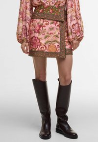 Short floral pink skirt with green trim and embroidery, paired with knee-high brown leather boots. Features a fitted silhouette and waistband.
