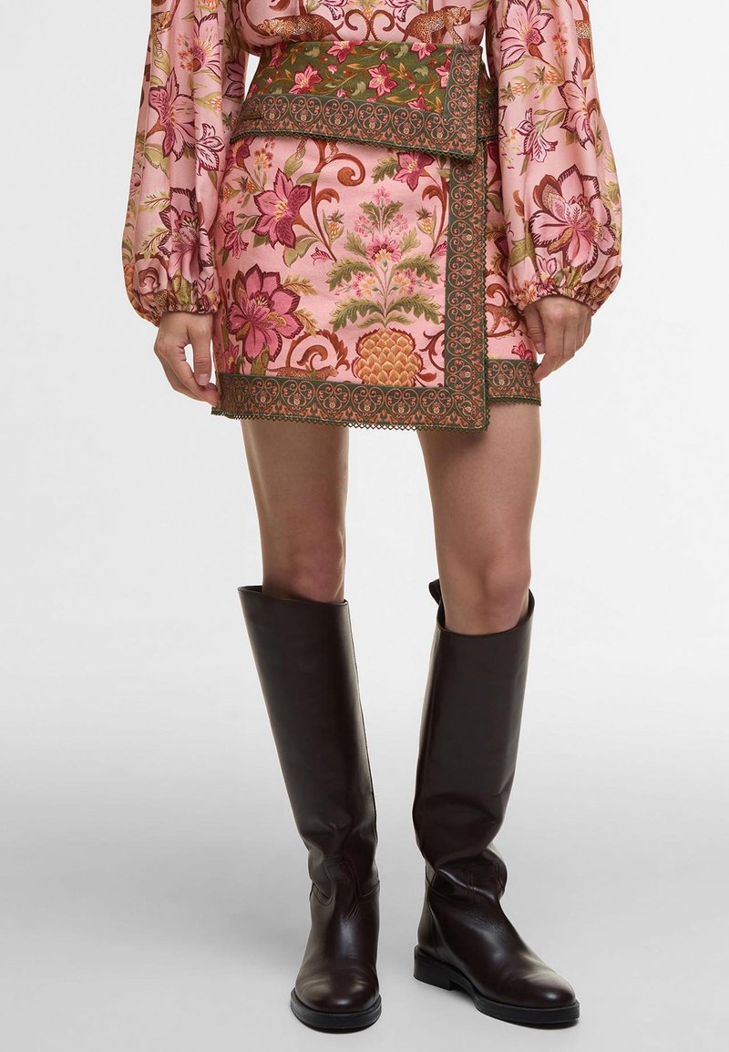 Short floral pink skirt with green trim and embroidery, paired with knee-high brown leather boots. Features a fitted silhouette and waistband.