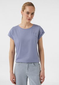 Helllila T-Shirt aus weichem Baumwollstoff mit umgeschlagenen kurzen Ärmeln. Verziert mit dekorativen Nähten in einem floralen Muster an der linken Schulter.