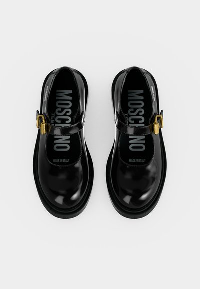 Paire de chaussures Mary Jane noires brillantes avec boucles dorées et marquage "Moschino" visible à l'intérieur, vues de dessus sur fond blanc.