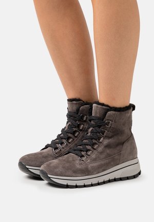 Grå ruskindsankelstøvler med sorte snørebånd og faux fur kant, der har en kraftig hvid sål og metalliske øjer. Det teksturerede materiale tilføjer dybde.