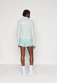 Minta zaļa sporta krekla ar garām piedurknēm ar balto Nike logotipu, kas saskaņots ar minta dzīvnieku raksta šortiem. Balti zeķes un sporta apavi noslēdz izskatu.