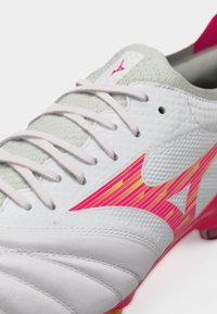 Λευκό και γκρι ποδοσφαιρικό παπούτσι με ροζ και πορτοκαλί ριγωτό λογότυπο στο πλάι, λευκά κορδόνια και κόκκινη εσωτερική επένδυση.