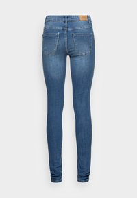 Skinny jeans in denim, medium blue color. Features a distinctive waistband with a tan leather patch, two back pockets with stitching details.