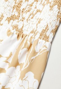 Robe fleurie avec un corsage smocké en blanc et beige, présentant un tissu texturé. Le bas a une finition lisse et légère avec des motifs floraux.
