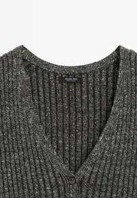 Pull en maille côtelée chinée gris foncé et blanc avec col en V et fermeture par un bouton noir unique.