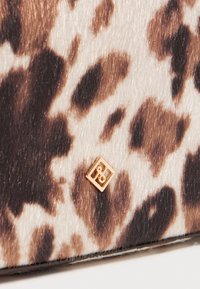 Luipaardprintstof met een zachte, textuurrijke oppervlakte in bruin en crèmetinten. Bevat een klein gouden logoaccent op de hoek.