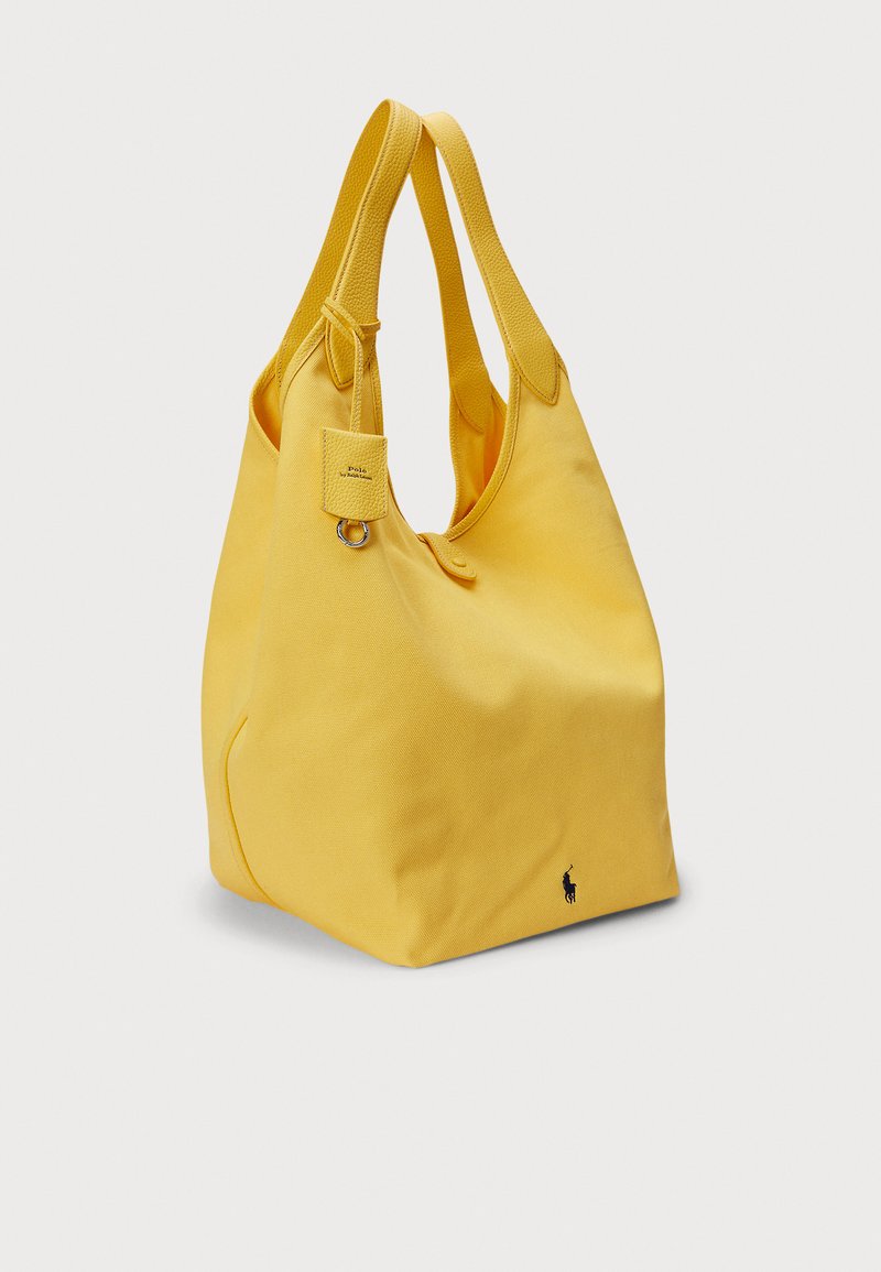 Yellow canvas tote bag with two textured handles, featuring a small label tag and a black logo on the lower side.