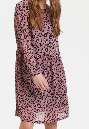 Woman wearing a pink, long-sleeve, knee-length dress with black leopard print, with loose, wavy brown hair partially visible.