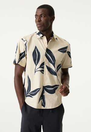 Camisa de manga corta en tejido beige claro con patrones de hojas azul oscuro, tapeta de botones y cuello abierto.