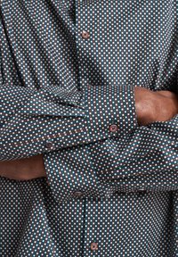 Mehrfarbiges Hemd mit einem kleinen quadratischen Muster in Türkis, Weiß und Braun. Gefertigt aus einem glatten Stoff mit Knopfdetails.