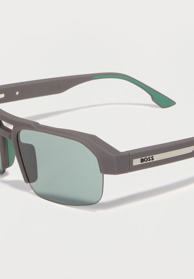 Lunettes de soleil rectangulaires BOSS grises avec verres teintés verts et accents verts sur les branches, affichant le logo BOSS sur les branches.