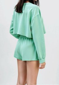 Felpa corta verde menta abbinata a pantaloni corti coordinati. Tessuto morbido, vestibilità ampia con vita elastica e dettagli a taglio vivo sui pantaloni.