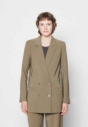 Double-breasted blazer in olive green fabric with notched lapels, two front pockets, and contrasting buttons. Styled over a dark top.
