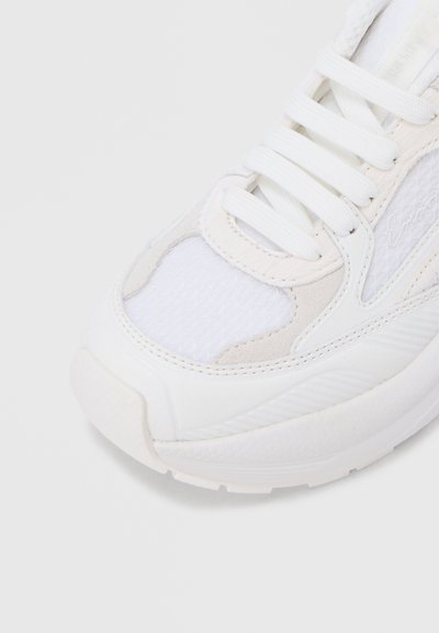 Λευκό αθλητικό παπούτσι με επικαλύψεις από δίχτυ και σουέντ, λευκά κορδόνια και υφή στην σόλα, σε κοντινή εικόνα από το δάχτυλο και πλάγια γωνία.