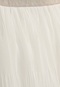 Weißer plissierter Rock mit strukturiertem Oberfläche. Besitzt einen gesmokten elastischen Bund, der weiche Falten über die gesamte Länge erzeugt.