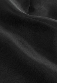 Schwarzer Satin-Stoff mit einer glatten, glänzenden Textur, die subtile Falten und einen sanften Glanz zeigt. Keine Muster oder Verzierungen sind sichtbar.