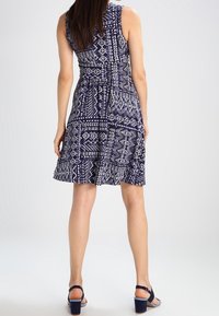 Navy blue patterned dress featuring a sleeveless design, flared skirt, and a textured fabric with geometric white accents.
