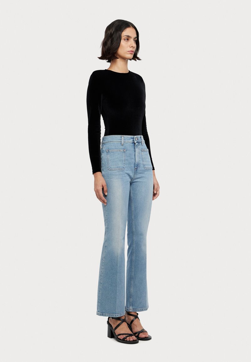 Svart fløyelslangermet topp sammen med lyseblå flagrende jeans med to frontlommer, teksturert stoff og svarte hælsandaler.