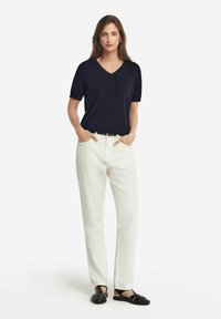 Mörkblå kortärmad V-ringad skjorta med avslappnad passform, i kombination med vita löst sittande byxor och svarta sandaler med flätad design.