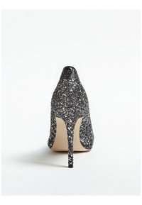 Zapato de tacón alto de glitter negro con punta afilada y tacón de aguja. Interior suave y un logo circular en la parte trasera.