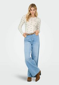 Langærmet crème top med blomstermønster, parret med højtaljede lyseblå vidde jeans. Brune hæle støvler supplerer outfittet.