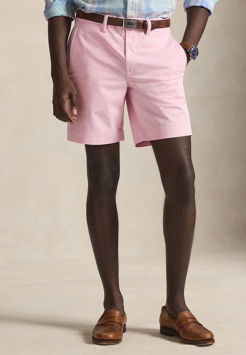 Rosa bomullsshorts med platt front, sidfickor och uppvikta kanter, kombinerade med bruna läderloafers och ett brunt bälte.