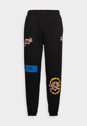 Pantalon de survêtement noir Adidas avec texte bleu « Adidas », graphique radio rose et jaune sur la cuisse gauche, et figure rose avec texte circulaire jaune sur la jambe droite.