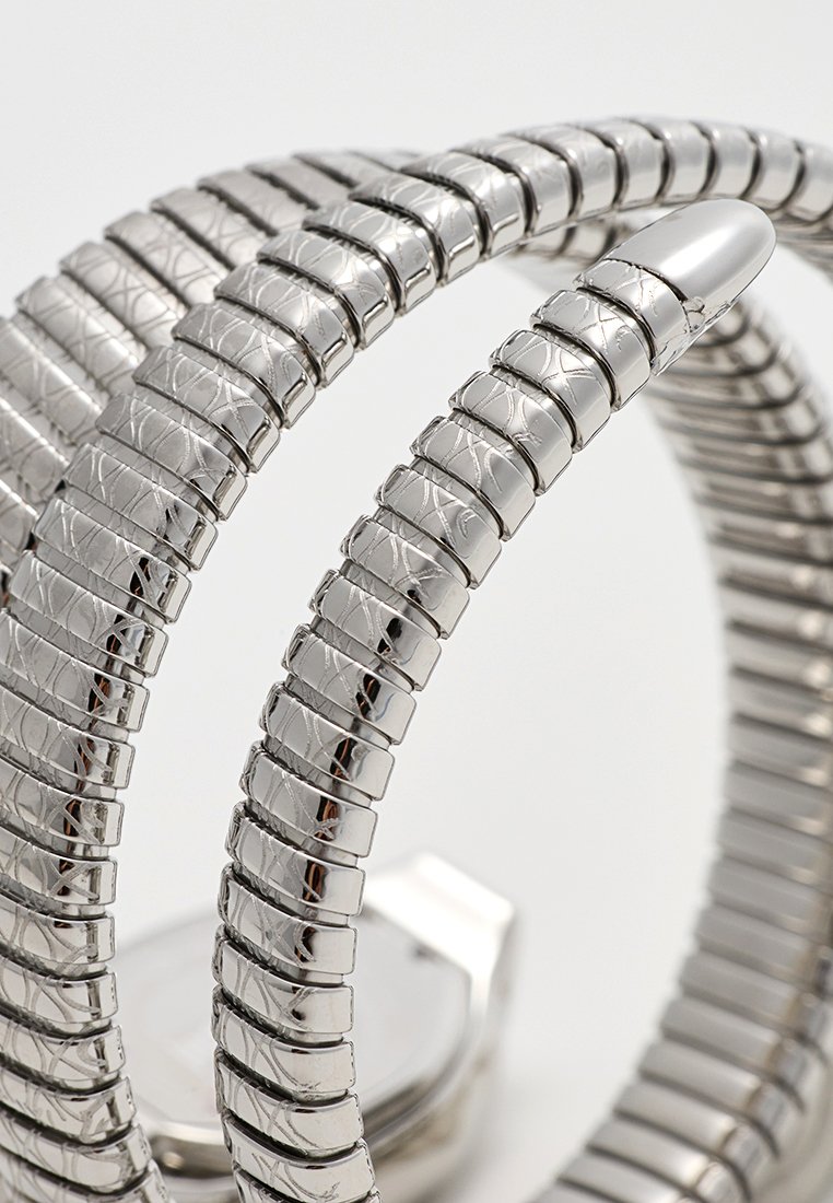 Reloj de pulsera plateado con una banda flexible compuesta de segmentos metálicos entrelazados, que presenta un patrón texturizado y una esfera de reloj rectangular.