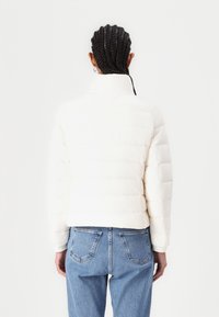 Witte pufferjack met een cropped ontwerp en een gewatteerde textuur. Heeft een hoge kraag en elastische manchetten, gecombineerd met blauwe jeans.