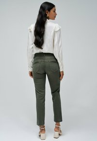 Blusa blanca de manga larga con hombros rizados, combinada con pantalones ajustados de color verde oliva, que cuentan con bolsillos traseros y un diseño de pierna afinada.