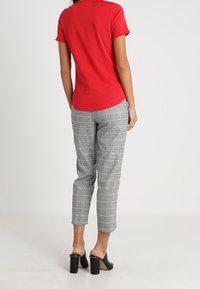 Camiseta roja de manga corta combinada con pantalones cortos de cuadros grises. Observar una textura suave y unos mules negros de tacón cuadrado.