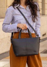 Borsa a mano in pelle nera con manici corti e tracolla staccabile. Texture liscia, forma rettangolare, con un logo sottile.