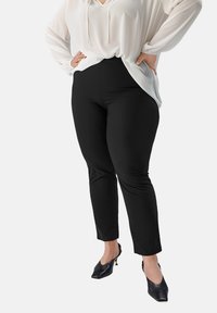 Zwarte, aansluitende broek met een gladde textuur, gecombineerd met een losse witte blouse. De outfit heeft een v-halsontwerp enGathered mouwen.