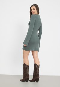 Abito a maglia a coste in verde tenue con maniche lunghe a campana, silhouette aderente e orlo svasato. Indossato con stivali cowboy marroni con tacchi decorati da ricami.