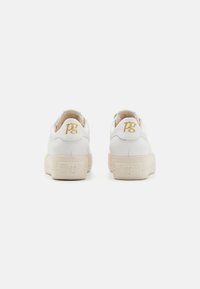 Des baskets blanches en cuir lisse avec un col rembourré, présentant une semelle texturée et un logo doré brodé sur le talon.