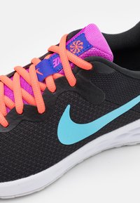 Chaussure de sport noire avec une tige en mesh, logo Swoosh turquoise, lacets rose et orange, et un talon en tissu texturé.