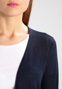 Navy blue knit cardigan with a v-neckline, worn over a white shirt. The fabric appears lightweight with a fine texture.