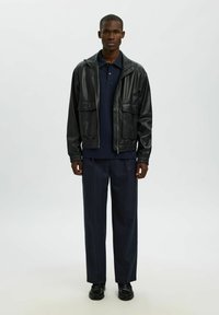 Črna usnjena jakna z dvema sprednjima žepoma, oblečena čez temno polo majico. V kombinaciji z morsko modrimi hlačami z ožjimi črtami in črnimi čevlji.