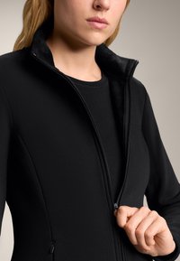 Czarna kurtka z zamkiem błyskawicznym i miękkim, pluszowym kołnierzem. Gładka faktura materiału z dopasowanym krojem. Detal zamka widoczny z przodu.