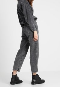 Czarne dżinsy z denimu o wysokim stanie i luźnym kroju, z efektem wyblakłym, pięcioma kieszeniami i przeszyciami, w połączeniu z czarnymi sznurowanymi botkami.