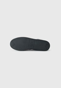 Semelle de chaussure en caoutchouc noir avec surface texturée, dotée d'un talon lisse et d'un logo en relief. Conçue pour l'adhérence et la stabilité.