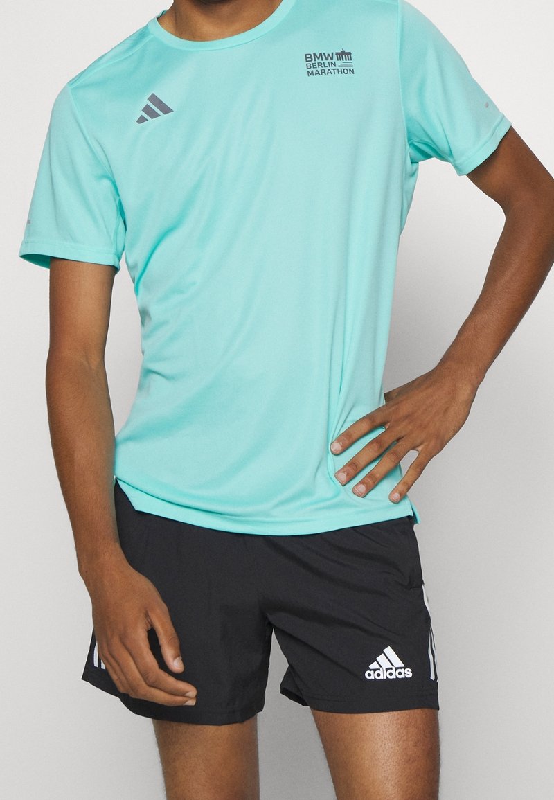 Světlemodré tričko s krátkým rukávem, které odvádí vlhkost, s šedým logem "BMW Berlin Marathon", spárované s černými šortkami se bílým logem Adidas.