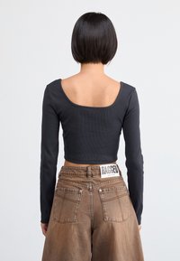 Black ribbed long-sleeve crop top with a wide scoop back, paired with high-waisted brown wide-leg jeans featuring patch pockets and a label.