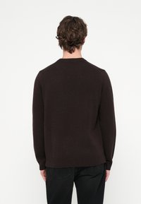 Barna kötött pulóver kerek nyakkal, hosszú ujjal és bordázott szegéllyel. Puha tapintású, egyszerű mintázatú, minimális díszítéssel és testhezálló szabással.