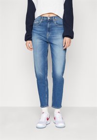 Vaqueros de mezclilla azul claro con un diseño de pierna recta y detalles ligeramente desgastados. Combinados con zapatillas blancas y un suéter de punto corto.