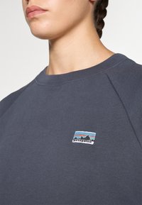 Sweatshirt de algodão cinza com decote arredondado e mangas raglan. Apresenta um patch do logótipo multicolorido da Patagonia no lado esquerdo do peito.