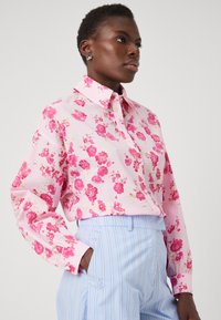 Blomstrete skjorte med knapper i lys rosa med røde og rosa blomster. Har krage, lange ermer og teksturert stoff.
