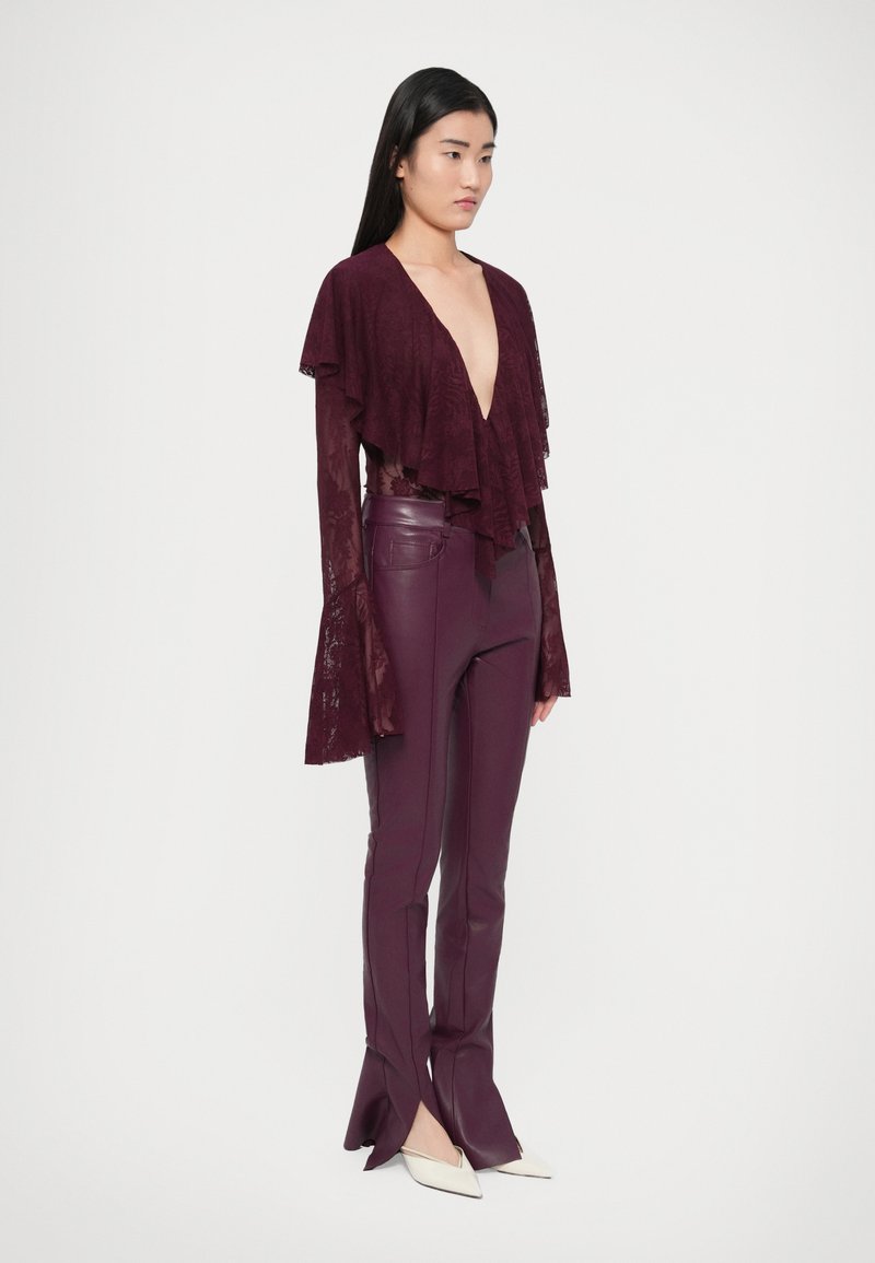 Bordeauxrode kanten top met gelaagde ruches en diepe V-hals, gecombineerd met nauwsluitende leren broek. Witte pumps met spitse neus maken de look af.